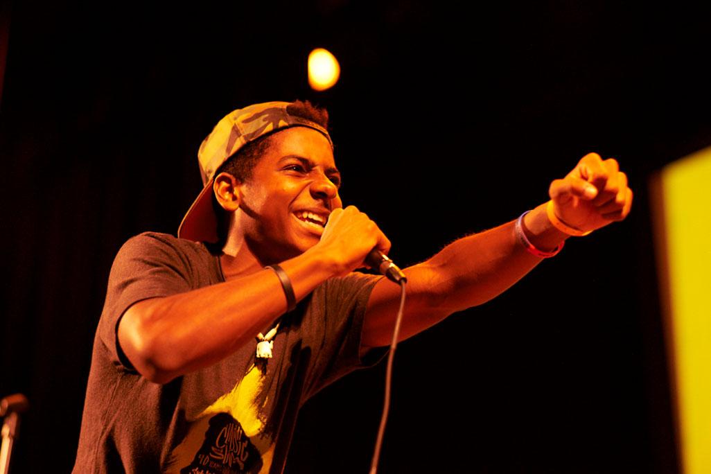 Image of performer on stage holding a fist up and speaking into a microphone