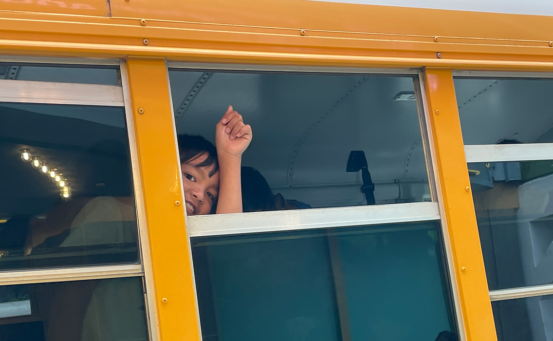A student on a school bus smiles and looks out the window