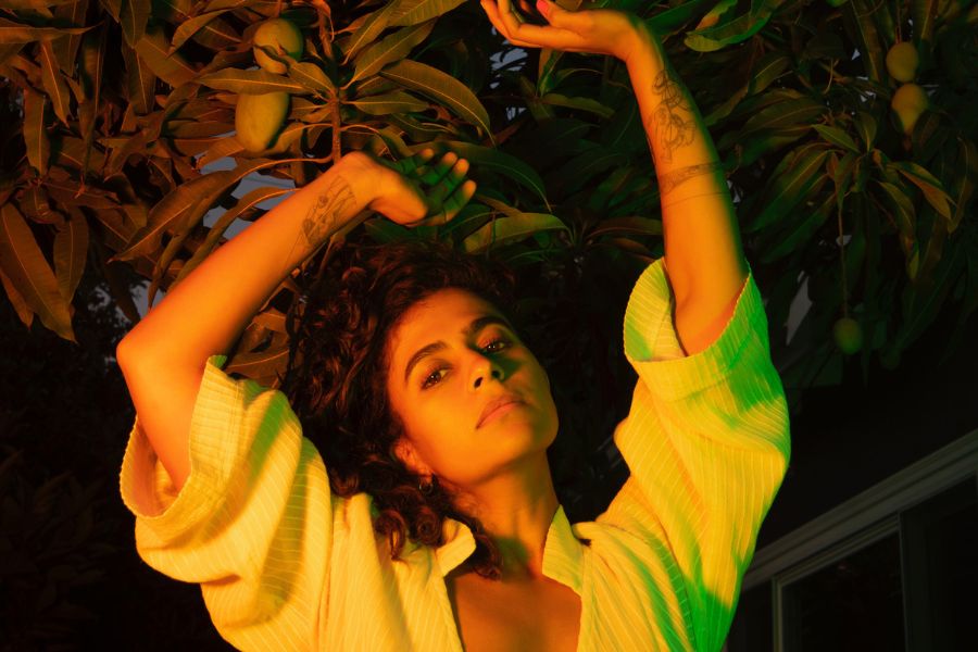 Madame Gandhi poses in green lighting in front of a plant