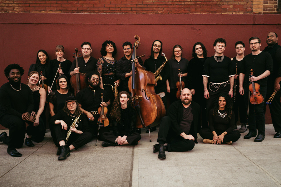 Group photo of performers from Wild Up posed in an outdoor setting, holding their respective instruments and wearing all black