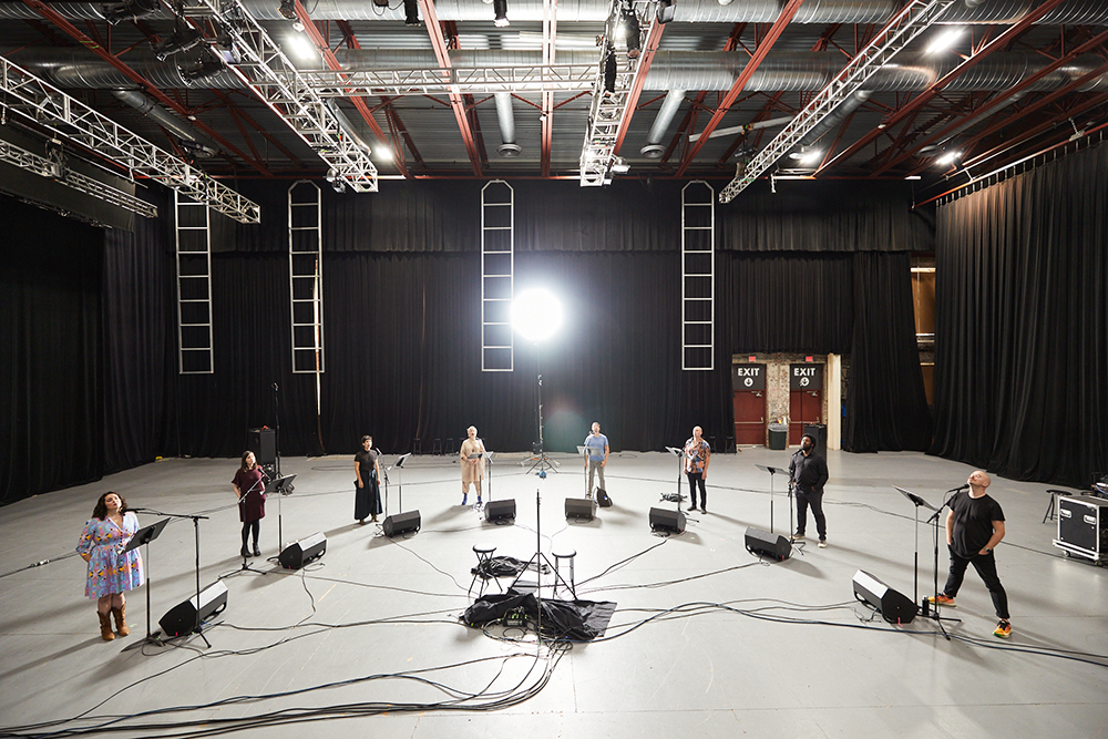 performers from Roomful of Teeth in a warehouse standing in a half circle with instruments
