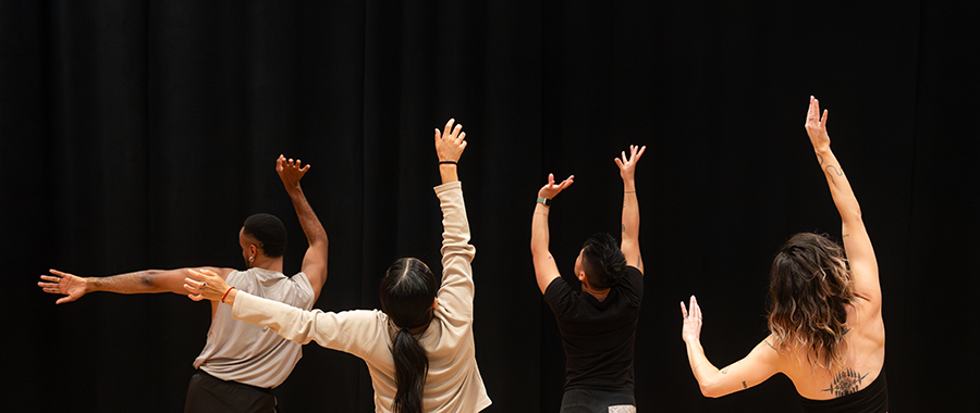 four performers on stage with hands outstretched amongst dark background