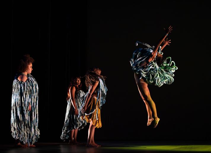 four dancers on stage in cultural dress with a black backdrop