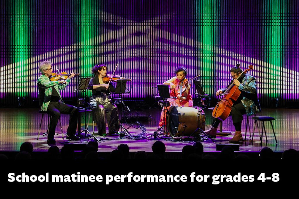 Members of Kronos quartet sitting beside one another with instruments playing while on a colorfully lit stage