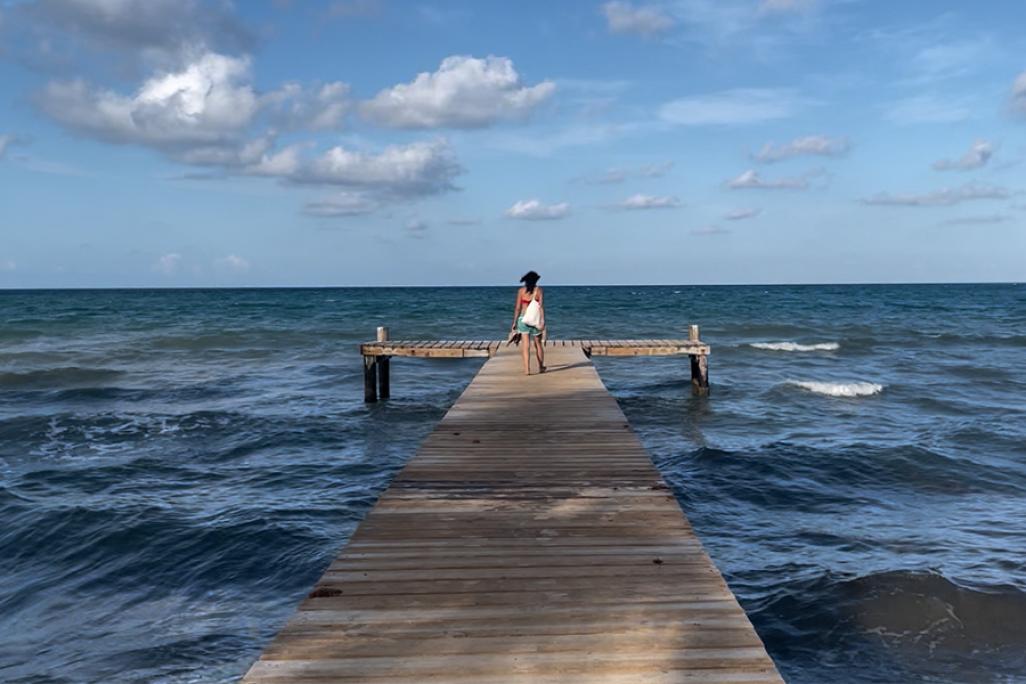 Image of a person standing on the middle of a dock looking out at the sea