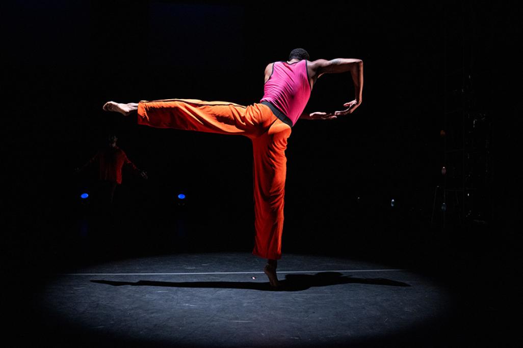 A performer dances on stage wearing orange and pink clothing
