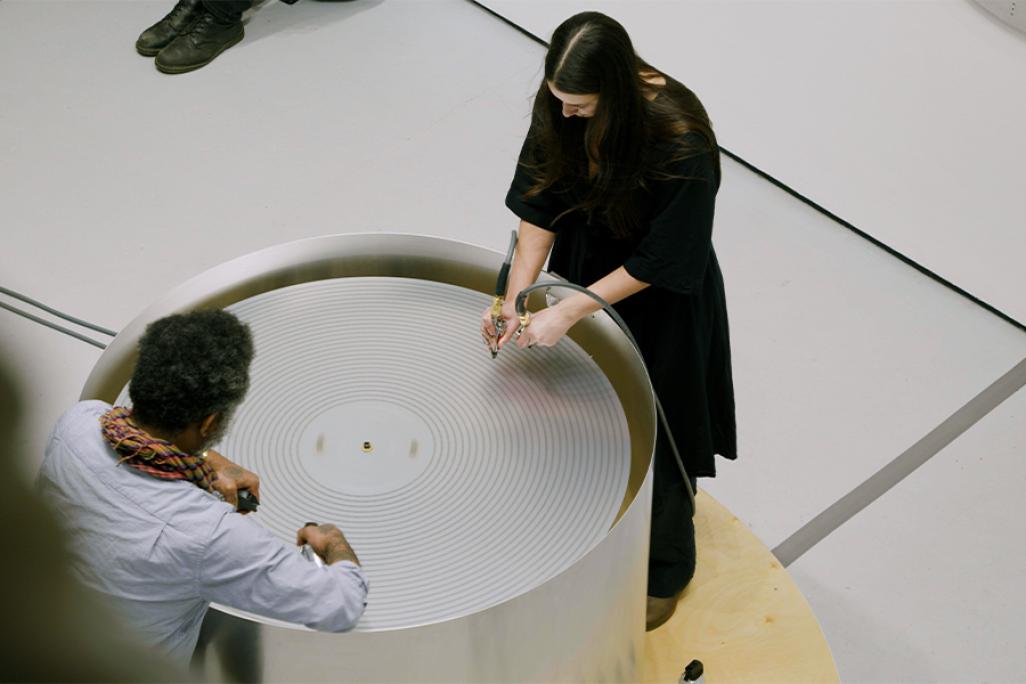 Photo taken overhead of two artists looking down at a circular machine