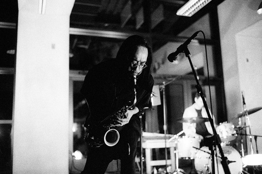 Black and white image of Patrick Shiroishi performing with a drummer in the foreground