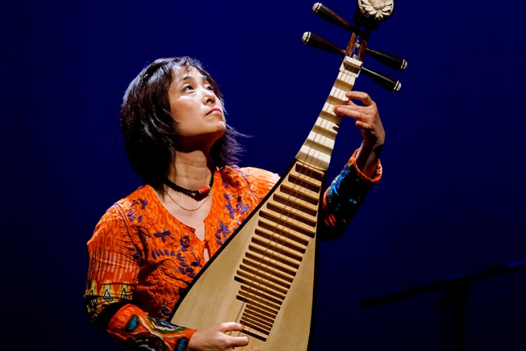 Wu Man performs on stage in front of a blue background