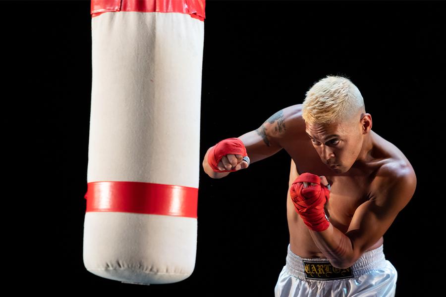 Image of Jay Carlon wearing boxing gloves, striking a punching bag