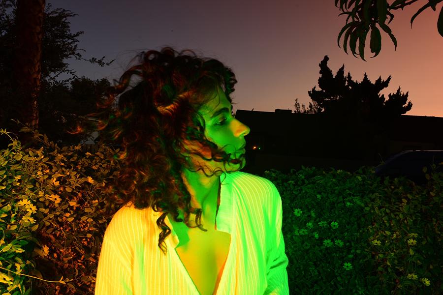 Madame Gandhi poses outdoors at night, lit by a green light