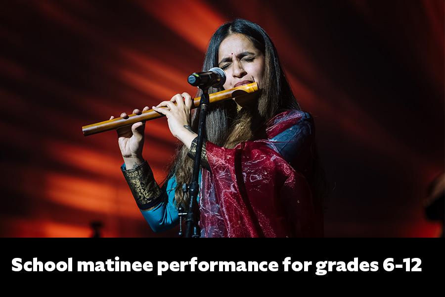 Artist Varijashree Venugopal playing a wood flute on stage dress in traditional clothing with red background