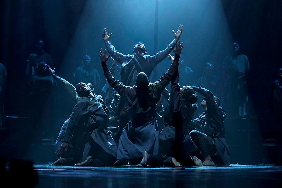 Dancers perform under a blue light in a pyramid formation
