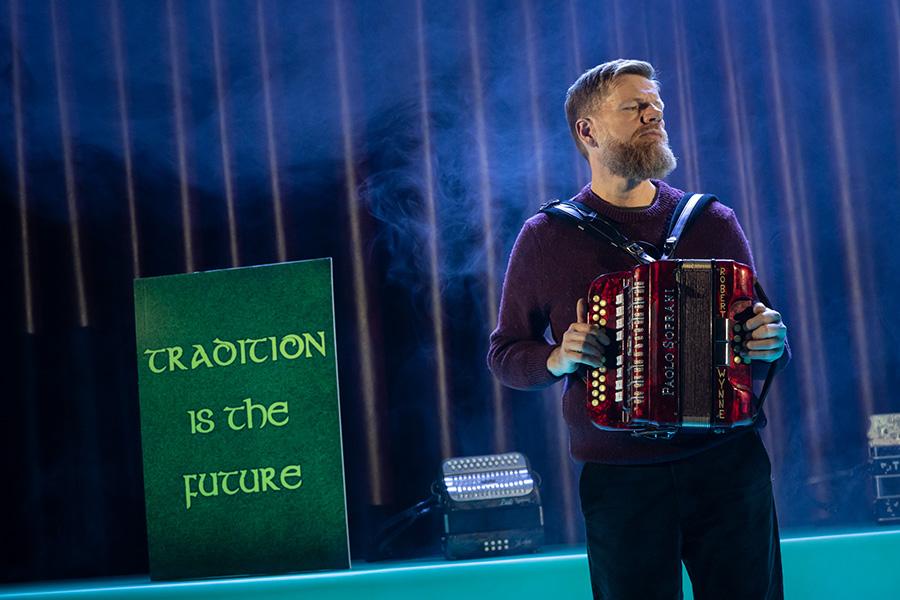 Man performs accordion on stage in front of a sign that reads 'Tradition is the Future'