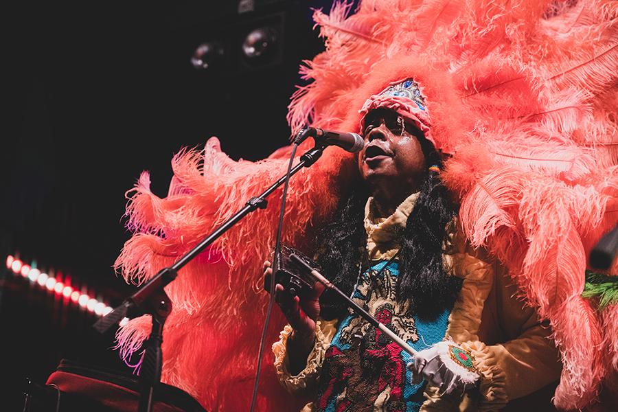 Monk Boudreaux performs on stage wearing large pink feather headpiece