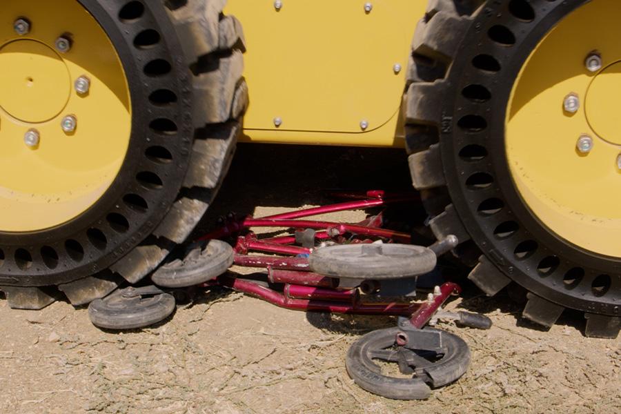 Image of truck wheels crushing a red wheelchair on a ground outdoor