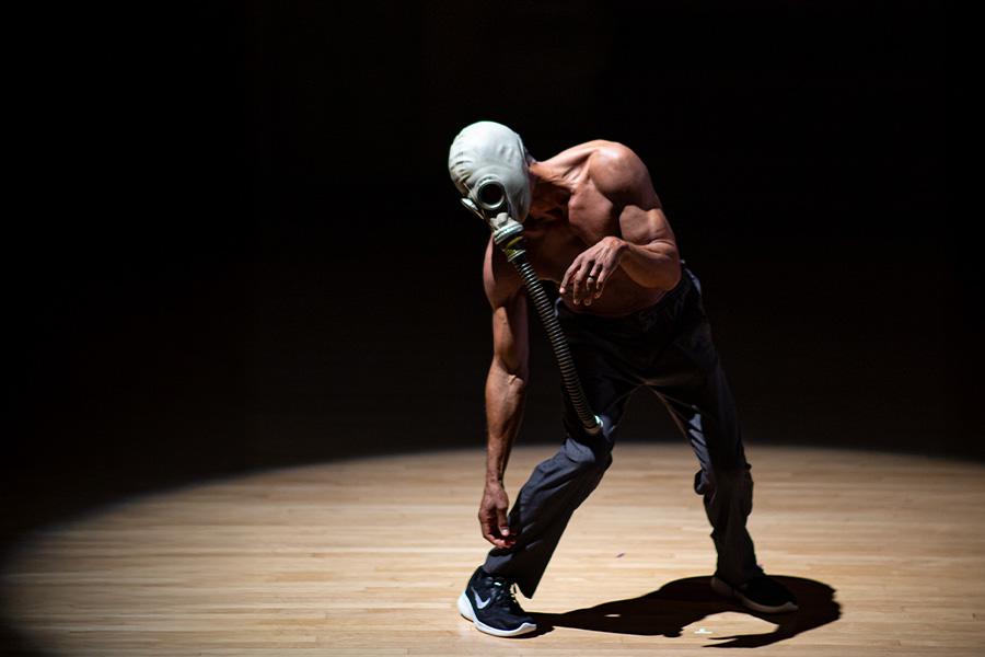 Performer poses in spotlight with mask on face