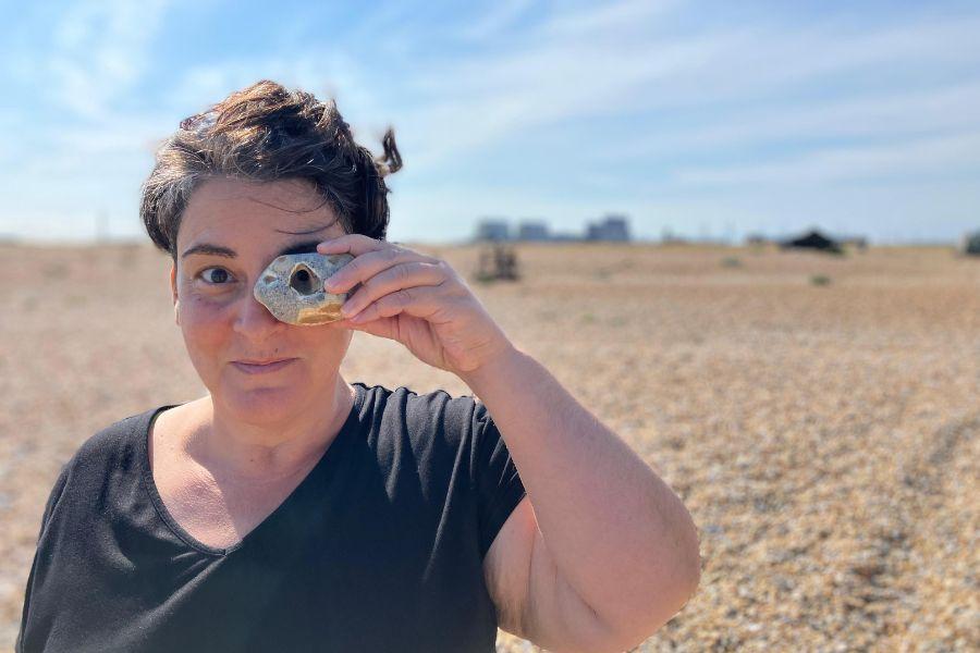 Image of Cassandra Miller standing in desert like landscape and holding a stone to their left eye