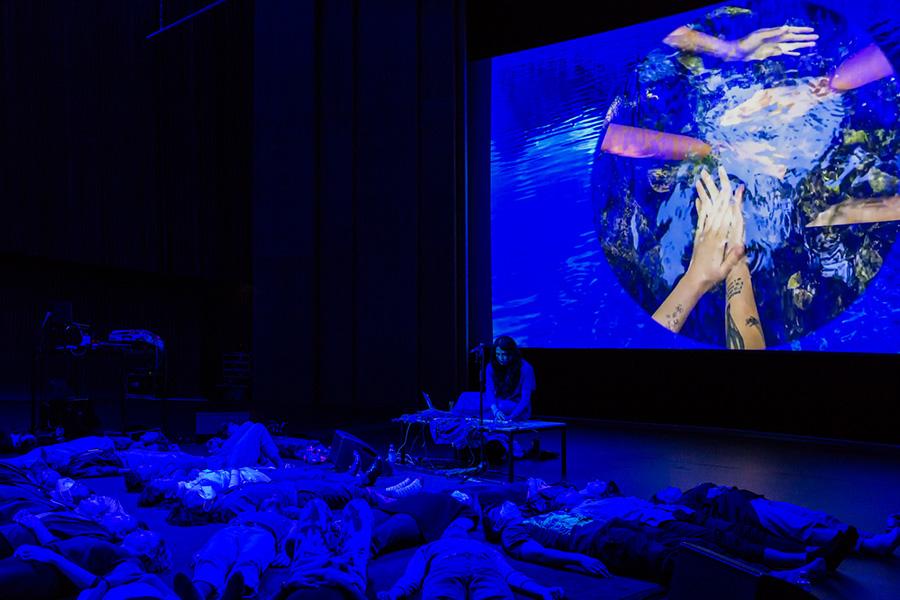 Image of people laying on floor while an image of hands is projected on screen