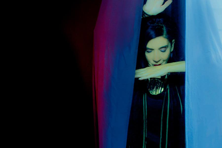 Sussan Deyhim poses with purple, blue, and red drapes around her
