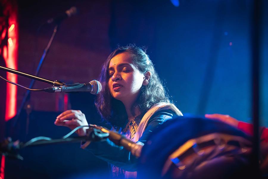 Close up, lower angle shot of Varijashree Venugopal performing on stage. Venugopal sings into a microphone with eyes closed, lifting one hand slightly as she sings.