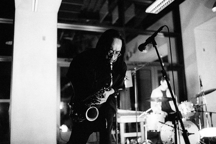 Black and white image of Patrick Shiroishi performing with a drummer in the foreground