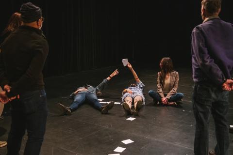 Performers holding note cards while laying on the ground
