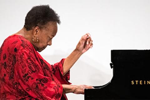Althea Waites sits and plays the piano in front of a white backdrop