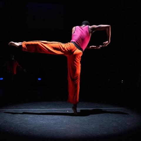 A dancer performs on stage wearing orange pains and a pink tank top