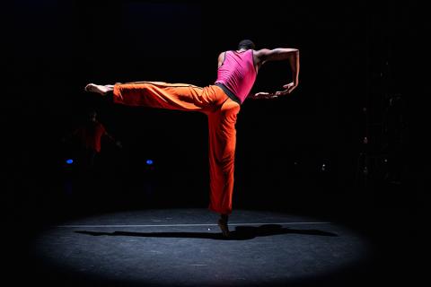 A performer dances on stage wearing orange and pink clothing