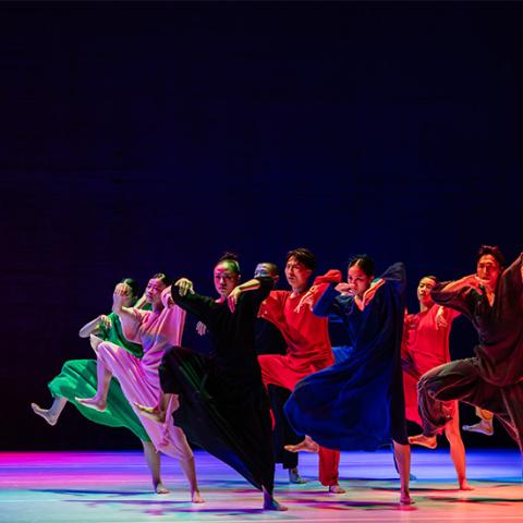 Image of dancers from Cloud Gate wearing colorful clothing, marching across stage