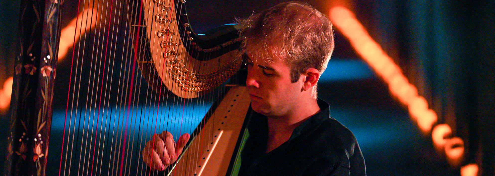Parker Ramsay wearing a black shirt playing the harp on stage with blue lighting