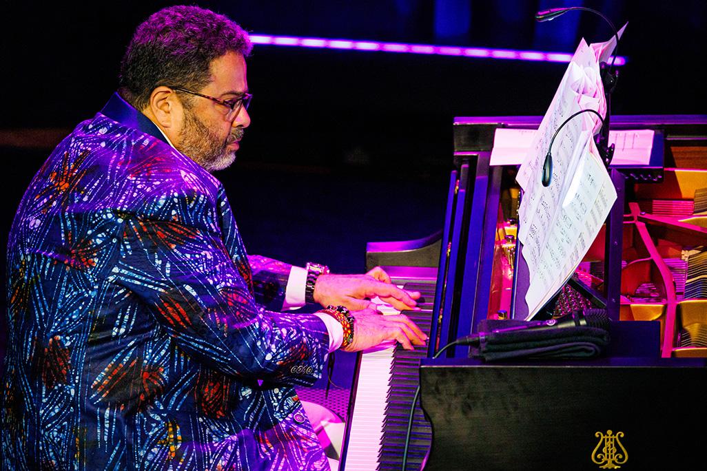 Arturo O'Farrill plays the piano on stage wearing floral suit jacket