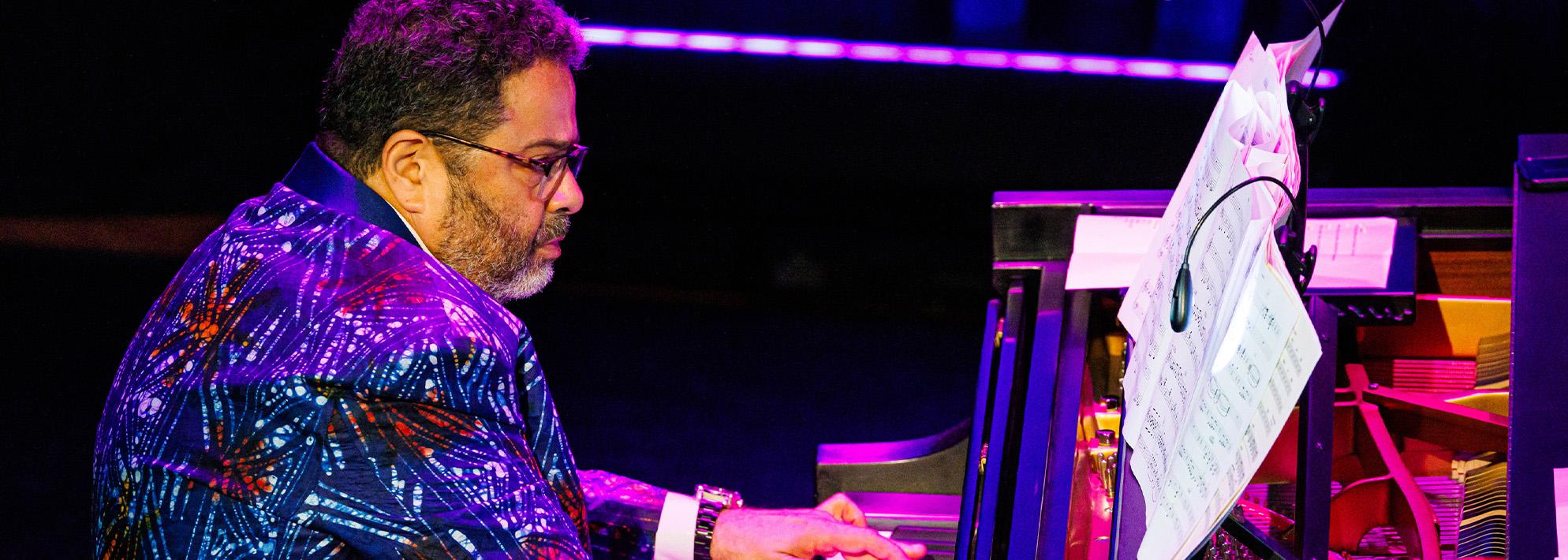 Arturo O'Farrill plays the piano on stage wearing floral suit jacket