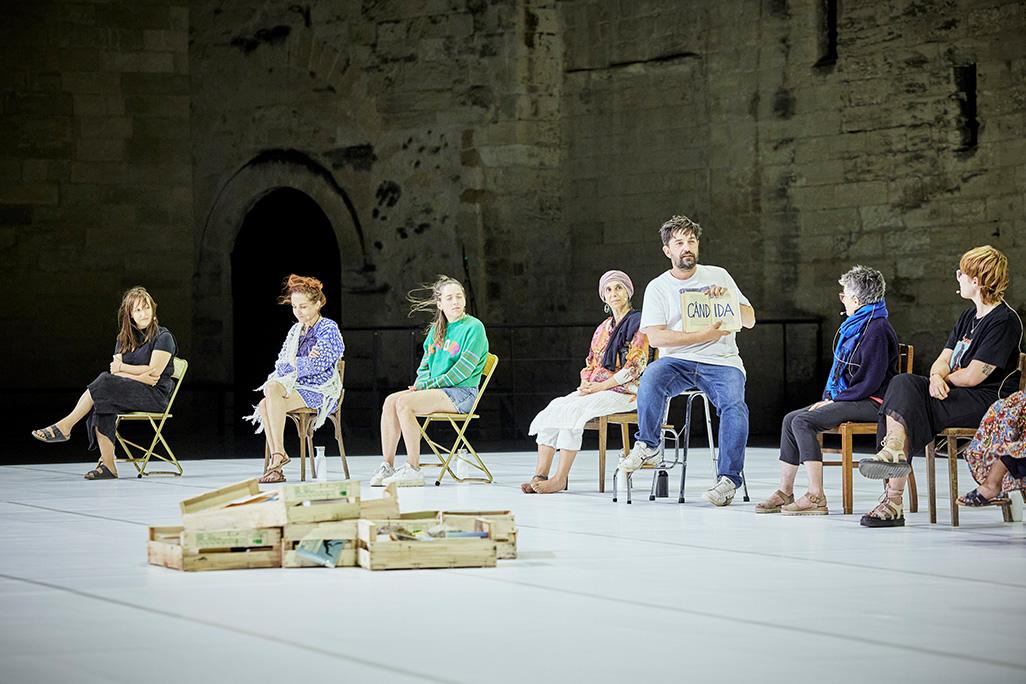 Tiago Rodrigues sits at a chair on stage holding a book with participants seated at separate chairs
