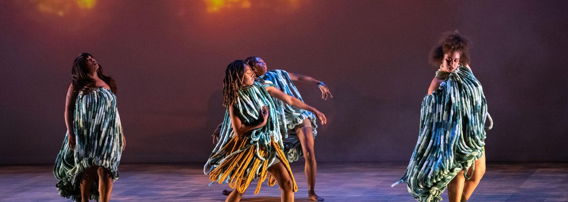Dancers perform on stage in front of a projection of trees