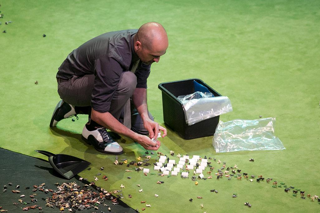 A performer crouches on stage and adjusts miniatures 