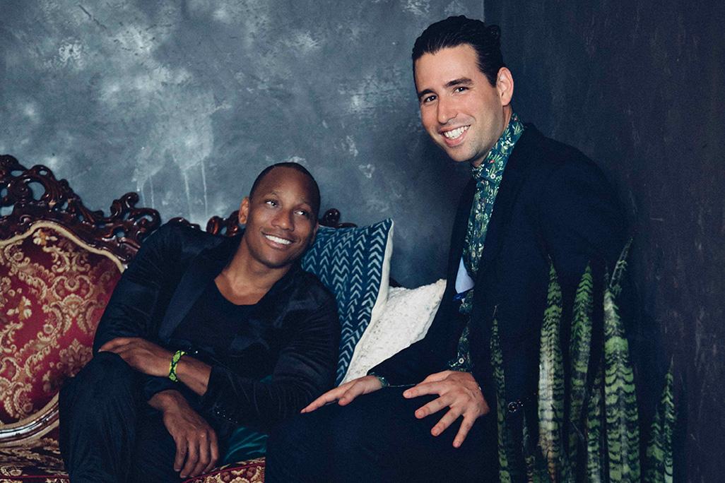 Pedrito Martinez and Alfredo Rodriguez smile and pose in front of a blue lime wash backdrop