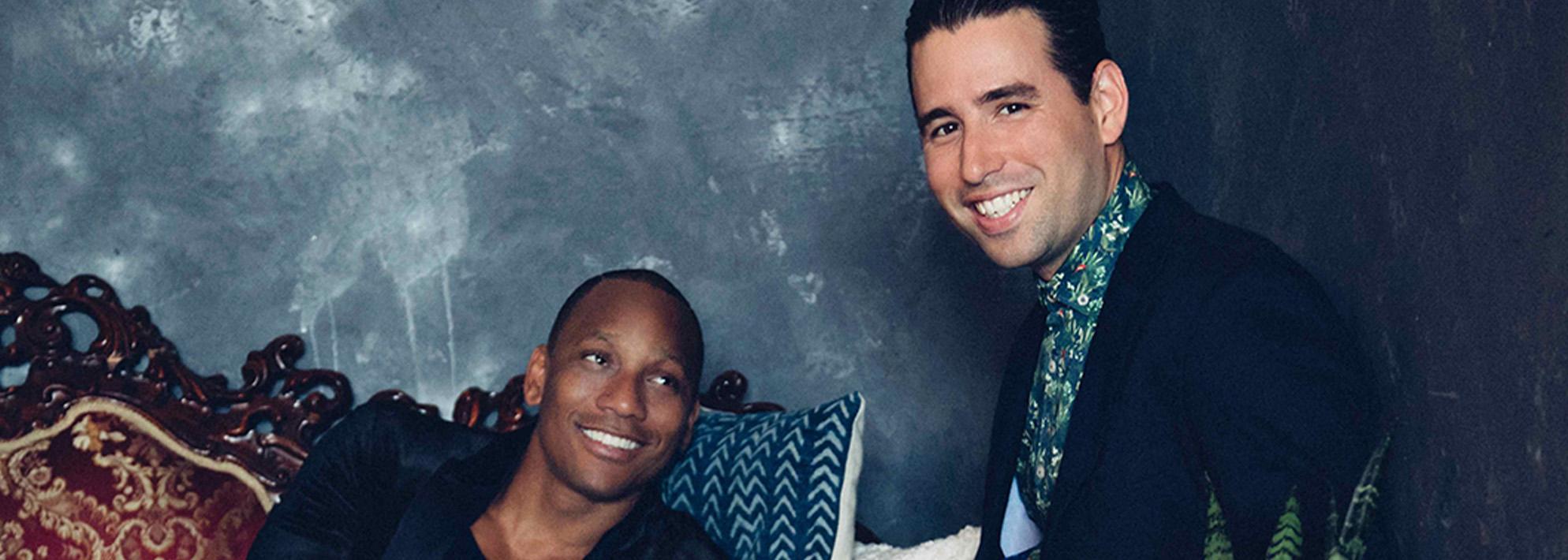 Pedrito Martinez and Alfredo Rodriguez smile and pose in front of a blue lime wash backdrop