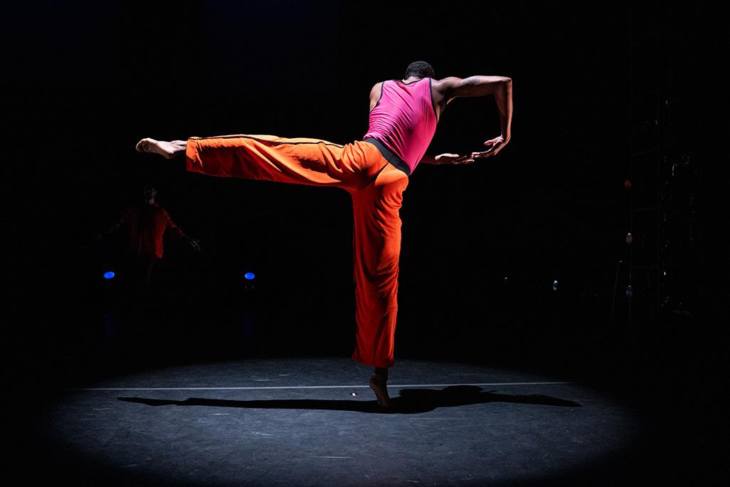 A performer from 'Still Here' performs on stage, facing backwards and lifting one leg in the air