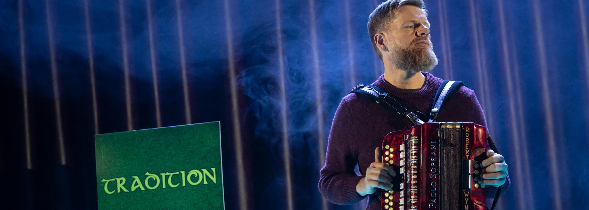 Danny O'Mahony plays the accordion on stage next to a sign reading 'tradition' to the left of him