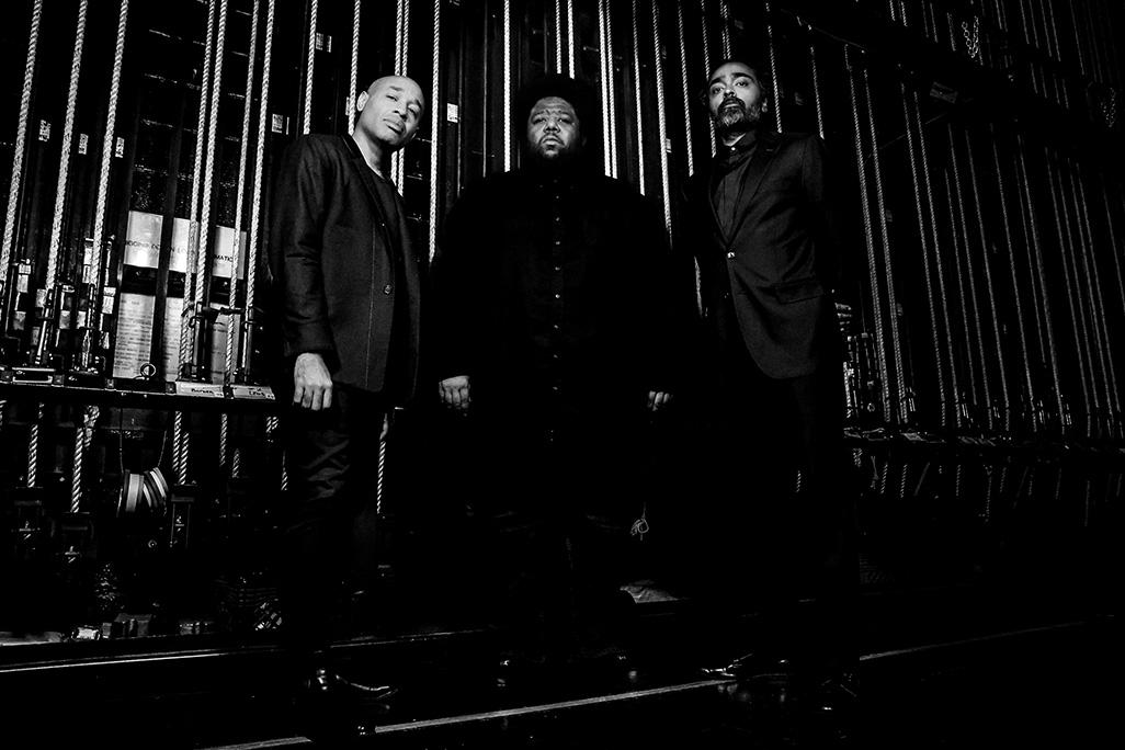 Black and white image of Tyshawn Sorey Trio posing backstage of a theater
