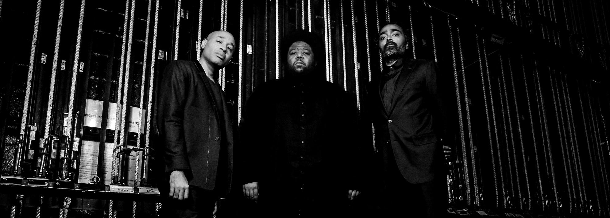 Black and white image of Tyshawn Sorey Trio posing backstage of a theater