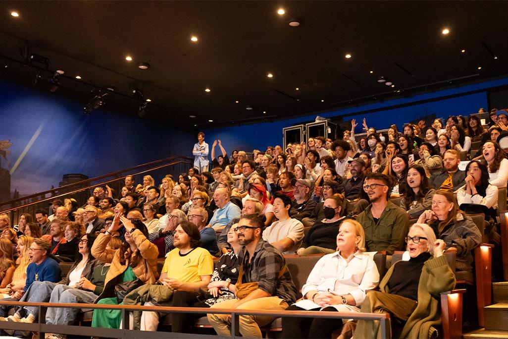 Audience members at The Nimoy sit in their seats and react with surprise and excitement at something happening off camera on the stage