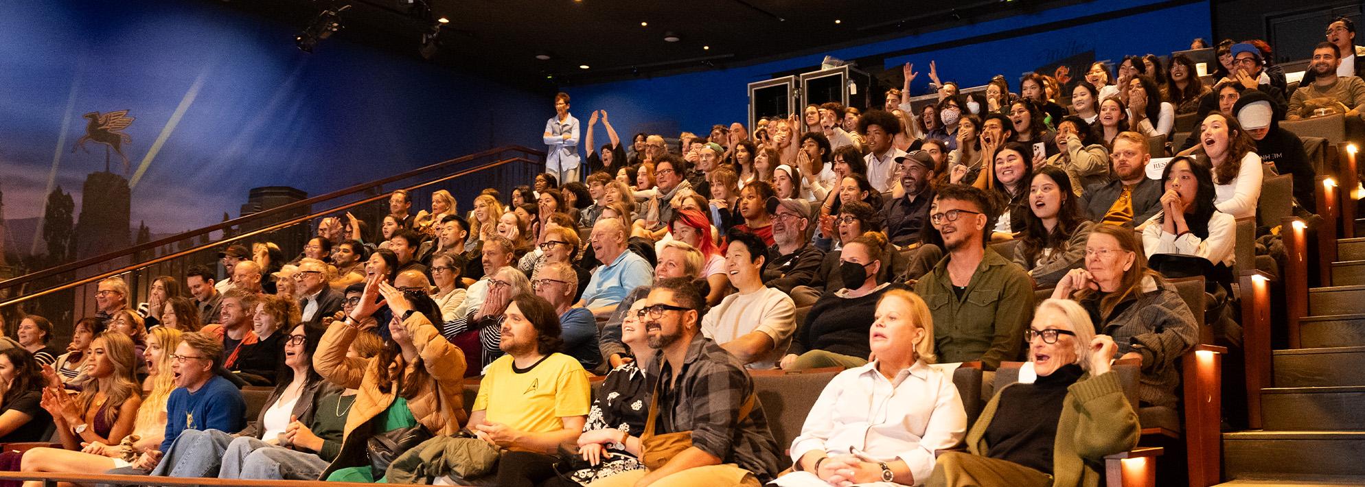 Audience members at The Nimoy sit in their seats and react with surprise and excitement at something happening off camera on the stage