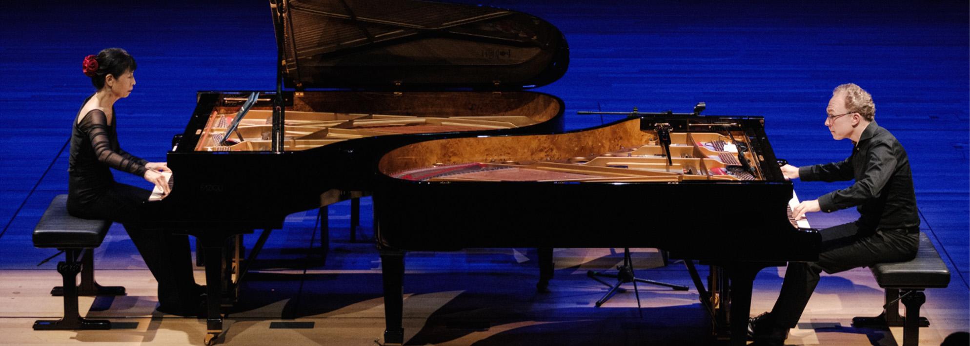 Ralph van Raat and Gloria Cheng perform on stage, seated at their respective pianos which are facing each other