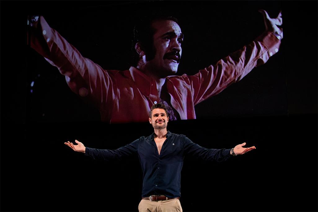 Javaad Alipoor performs on stage with an image of Fereydoun Farrokhzad projected on screen behind him